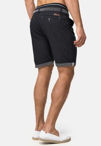 Sorte shorts med et tekstureret mønster, opfoldede manchetter og en kontrastfarvet talje. Har to baglommer og et læderdetalje.