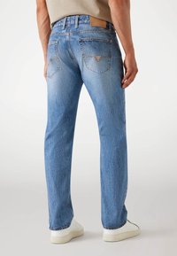 Lichtblauwe denim jeans met een rechte fit, voorzien van een leren Guess-label op de tailleband en zichtbare stiksels op de achterzakken.