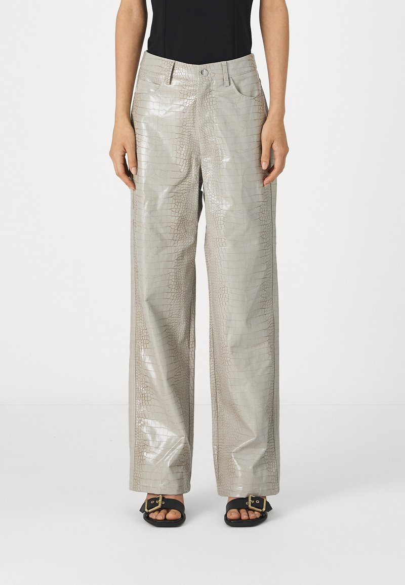 Γκρίζες, γυαλιστερές παντελόνες σε στυλ κροκοδείλου με φαρδιά πόδια, μπροστά τσέπες και κουμπί κλεισίματος, συνδυασμένες με μαύρες σανδάλια που έχουν χρυσές λεπτομέρειες.