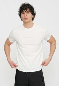T-shirt bianca a maniche corte con collo rotondo, realizzata in tessuto liscio. La vestibilità è aderente, presentando un design pulito e minimalista.