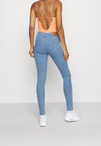 Jeans de denim azul ajustados con bolsillos traseros, cintura alta y una etiqueta de cuero. Combinados con un body naranja y zapatillas blancas.