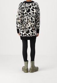 Pull en tricot avec un imprimé léopard noir et blanc, des manches larges et un ourlet noir côtelé. Associé à des bottines vert olive et des leggings noirs.