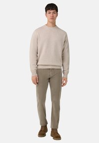 Beżowy sweter z dzianiny z okrągłym dekoltem, zestawiony z jasnoszarymi spodniami z sztruksu i brązowymi butami na sznurowadła, stojący na jednolitym tle.