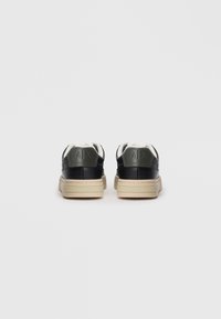 Zwarte en groene leren sneakers met een beige zool, voorzien van een gestructureerd achterpaneel en witte veters. Logo in de hiel geperst.