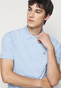 Light blue short-sleeve polo shirt with a collar, featuring a three-button placket and a small embroidered design on the chest.