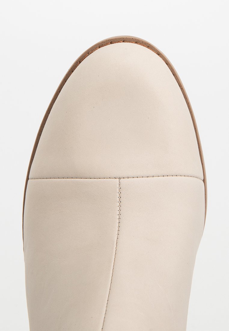 Beige Leder-Ankle-Boot mit runder Zehenform, glatter Textur und minimalistischem Nähdetail, ausgestattet mit einer kontrastierenden, hellbraunen Sohle.