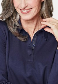 Marineblaues Langarm-Polohemd mit Kragen, ausgestattet mit einer Knopfleiste und strukturiertem Stoff. Das Hemd hat blaue Knöpfe und eine weiche Oberfläche.