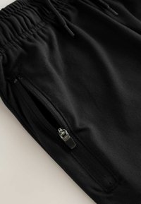 Czarne spodnie dresowe z elastycznym pasem i zasuwaną kieszenią boczną, charakteryzujące się gładką fakturą i minimalistycznym designem.