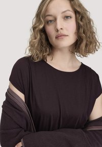 Korte mouw, diep paarse top met een gladde textuur, gecombineerd met een donkere, zacht gelaagde cardigan met een rits.