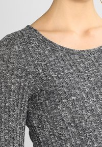 Maglia a coste grigia con scollo ampio, texture media e motivo sottile. Presenta maniche lunghe e una silhouette aderente.