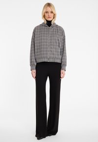 Veste zippée grise avec un motif en grille, équipée d'une capuche et de poignets élastiques, associée à un pantalon large noir. Texture lisse sur l'ensemble.