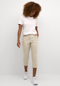 Beige cropped pants with a straight cut, featuring belt loops and side pockets, paired with a plain white t-shirt and white sneakers.