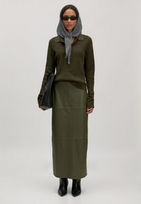 Olijfgroene trui met studs op de kraag, gecombineerd met een bijpassende leren rok. Accessoires zijn een grijze sjaal en een zwarte tas. Zwarte gemarkeerde laarzen.