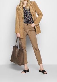 Tan corduroy blazer, floral navy top, beige slim-fit trousers, brown leather tote bag, and black slide sandals with low heels.