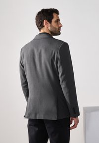 Grå strukturerad kavaj med en enda slits, skräddarsydd passform och notch-lapel. Tyget har en subtil textur, kompletterad med knappdetaljer på ärmarna.