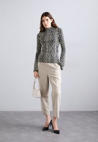 Un col roulé ajusté à rayures noires et crème, un pantalon beige ajusté, des escarpins noirs en vernis et un petit sac à main clair avec un logo.