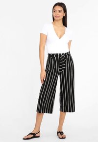 Mustad vertikaalsete valgete triipudega culottes-püksid, millel on kõrge vöökoht ja lipsuga vöö. Ühildatud valge liibuva V-kaelusega topi ja sandaalidega.