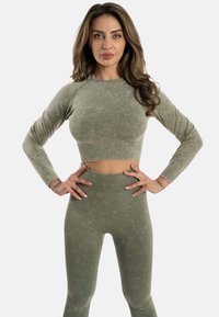 Set di abbigliamento attivo verde oliva composto da un top corto a maniche lunghe e leggings a vita alta. Tessuto morbido con dettagli a coste e design seamless.