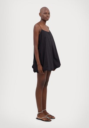 Čierne bezrukávové šaty s voľným strihom, vyrobené z hladkej látky. Obsahujú tenké ramienka a zaoblený lem. Skombinované so striebornými sandálmi.