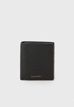 Portefeuille en cuir noir avec finition texturée, design à rabat, et détail en relief "Calvin Klein" sur le bas à l'avant. Forme compacte et élégante.
