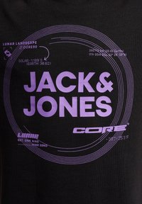 Svart bomull t-skjorte med kraftig lilla trykk med "JACK & JONES" og sirkulære grafiske design, inkludert tekst og symboler.