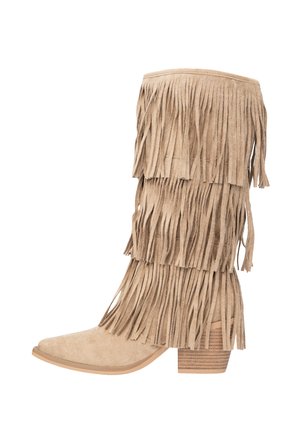 Bota de ante beige con detalle de flecos en capas, punta puntiaguda y tacón apilado. La textura es suave y el diseño es alto y ajustado.