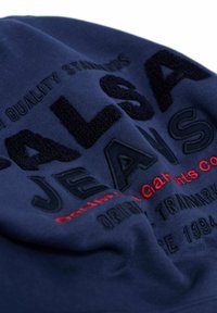 Camiseta de tejido azul marino con bordado texturizado en negro y rojo del texto "SALSA JEANS" y texto adicional, creando un efecto de diseño en capas.