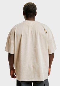 Rövid ujjú, oversized bézs T-shirt, puha tapintással. Kerek nyakkivágással és laza szabással rendelkezik, látható márka vagy kiegészítők nélkül.