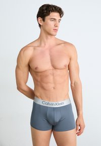 Boxers de hombre en gris con una textura suave y un logotipo de Calvin Klein en plateado contrastante en la cinturilla. Diseño ajustado.