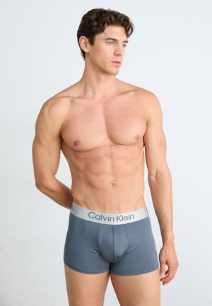 Férfi szürke boxeralsó, sima textúrával és kontrasztáló ezüst Calvin Klein logóval a derékszíj alatt. Formázott dizájn.