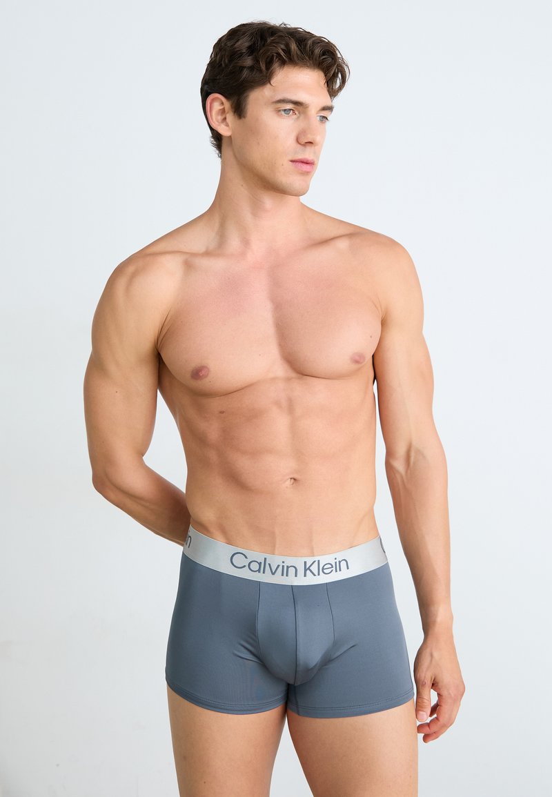 Boxers de hombre en gris con una textura suave y un logotipo de Calvin Klein en plateado contrastante en la cinturilla. Diseño ajustado.