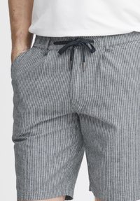 Grå og hvite stripete shorts med snor i livet, sidelommer og en avslappet passform. Stoffet ser teksturert og lett ut.