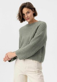 Maglione a maglia verde oliva con texture a coste, collo a giro, e vestibilità ampia. Presenta maniche lunghe e una silhouette rilassata.