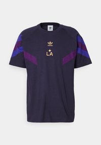 Laivansinis puuvillainen t-paita lyhyillä hihoilla, jossa on purpleja ja sinisiä kulmatyylisiä yksityiskohtia olkapäillä sekä kultainen teksti "LA". Adidas-logo ylhäällä.