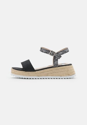 Sandalia espadrille negra con una correa ancha, correa para el tobillo con estampado, cuña cubierta de yute y suela de goma blanca texturizada.