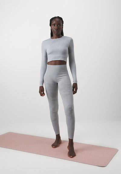 Light gray long-sleeve crop top and high-waisted leggings with a subtle pattern, worn with bare feet on a light pink yoga mat.
