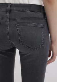 Jeans di denim grigio scuro con un design aderente, dotati di una tasca posteriore e discreti dettagli di cucitura. La cintura presenta un'etichetta nera.