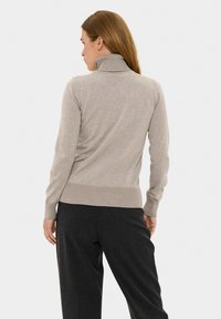 Pull en col roulé beige avec un col et des poignets côtelés, en tissu tricoté léger, au design ajusté, associé à un pantalon noir ajusté.