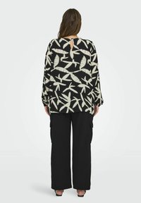 Blusa negra con patrón de hojas crema, con mangas largas y detalle de ojal en la espalda, combinada con pantalones cargo negros de pierna ancha.