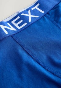 Boxer shorts en coton bleu avec une large ceinture élastique portant le nom de la marque "NEXT" en blanc. Texture lisse et design ajusté.