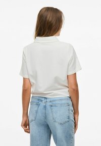 Polo shirt bianco a maniche corte con una texture morbida, caratterizzato da un colletto classico, abbinato a jeans a vita alta di colore azzurro chiaro e dalla vestibilità comoda.