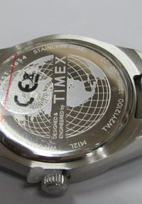 Fond de montre en acier inoxydable avec un design de globe, gravé avec "TIMEX," marque de certification et numéro de modèle ; texture métallique visible.