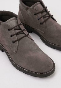 Botas de tobillo de ante gris con puntera redondeada. Presentan cordones marrones, ojales y una suela texturizada. Costuras en contraste a lo largo del borde.