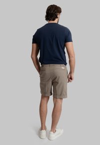 T-shirt a maniche corte blu navy abbinato a pantaloni corti color marrone chiaro, presenta un orlo arrotolato, una vita elastica e sneakers bianche.