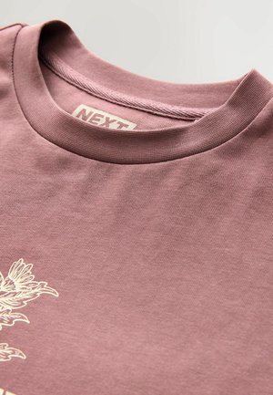Kortærmet mauve T-shirt lavet af bomuld, med runde halsudskæring og et trykt design på forsiden. Etikettet er synligt indeni halsen.