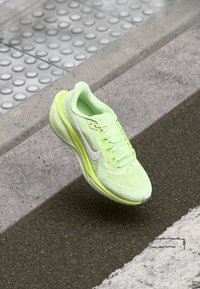 Zapatilla de correr de color amarillo neón con parte superior de malla, cuello acolchado y un swoosh de Nike en blanco reflectante. Diseño ligero con suela texturizada.