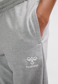 Graue Sweatpants aus weichem Material, mit einer seitlichen Tasche und gesticktem "hummel"-Logo in Weiß am unteren Bein.
