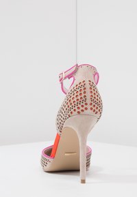 High-heeled shoe in beige suede with cut-out design, pink accents, and orange inner lining. Features a slim heel and adjustable ankle strap.