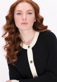 Cardigan blu navy con accenti crema, texture a coste e scollatura tonda. Presenta cinque bottoni neri e argento lungo la parte anteriore.
