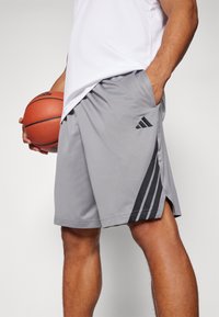Calções de basquetebol cinzentos com riscas pretas, bolsos laterais e uma cintura elástica. Feitos de material leve e que afasta a humidade.